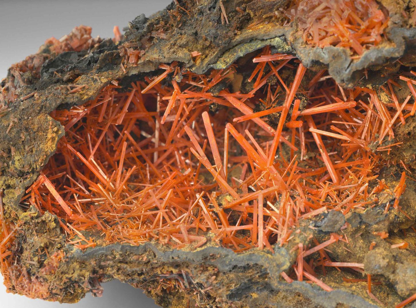nadelige, orangerote Krokoitkristalle stehen in einer kleinen Kristalldruse