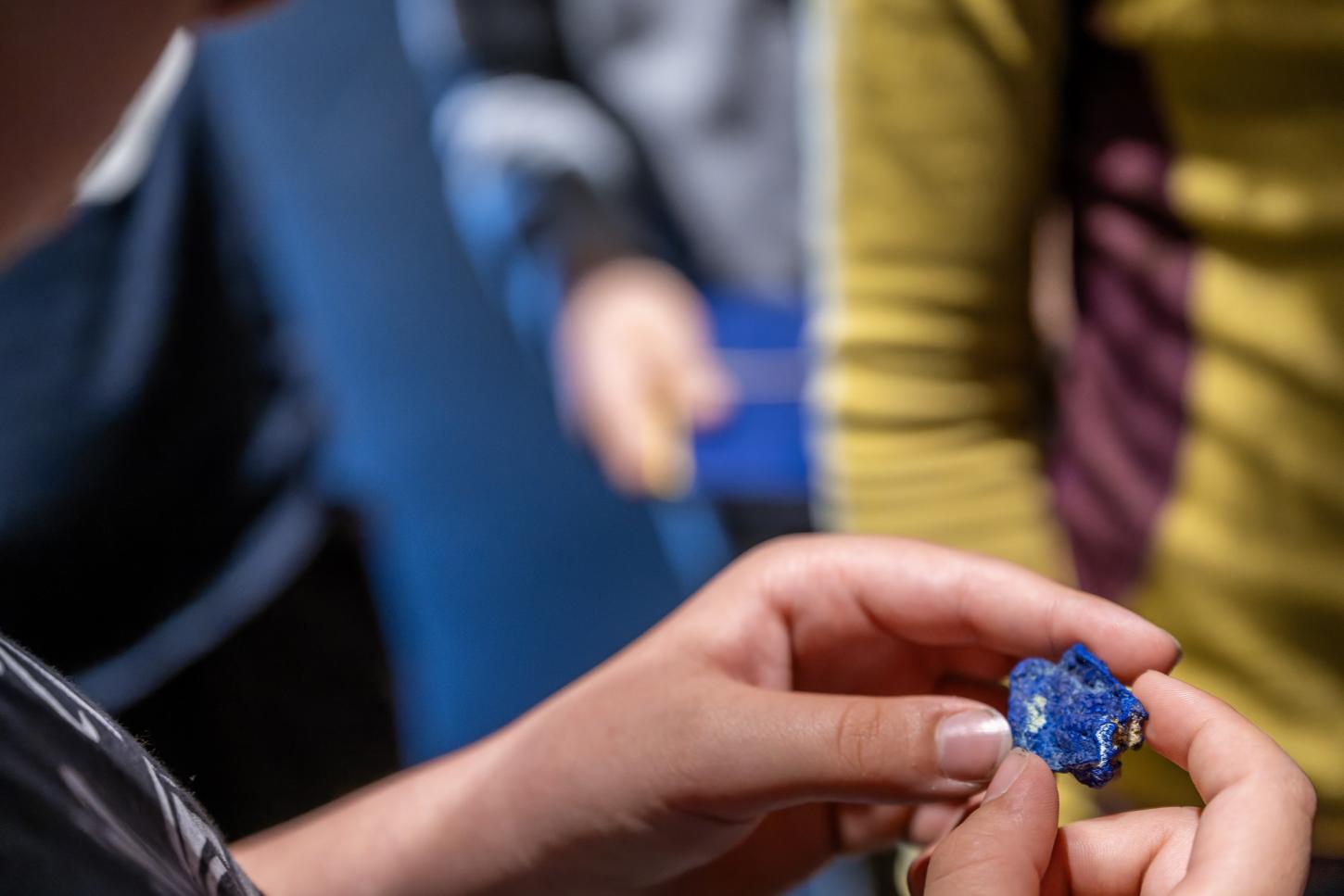 Ein Kind hält ein kleines, blaues Mineral zwischen den Fingern seiner beiden Hände.