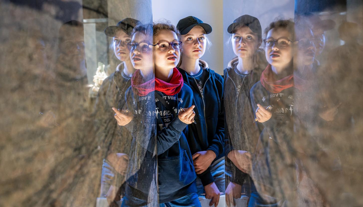 Zwei Kinder spiegeln sich staunend in polierten Gesteinsplatten.